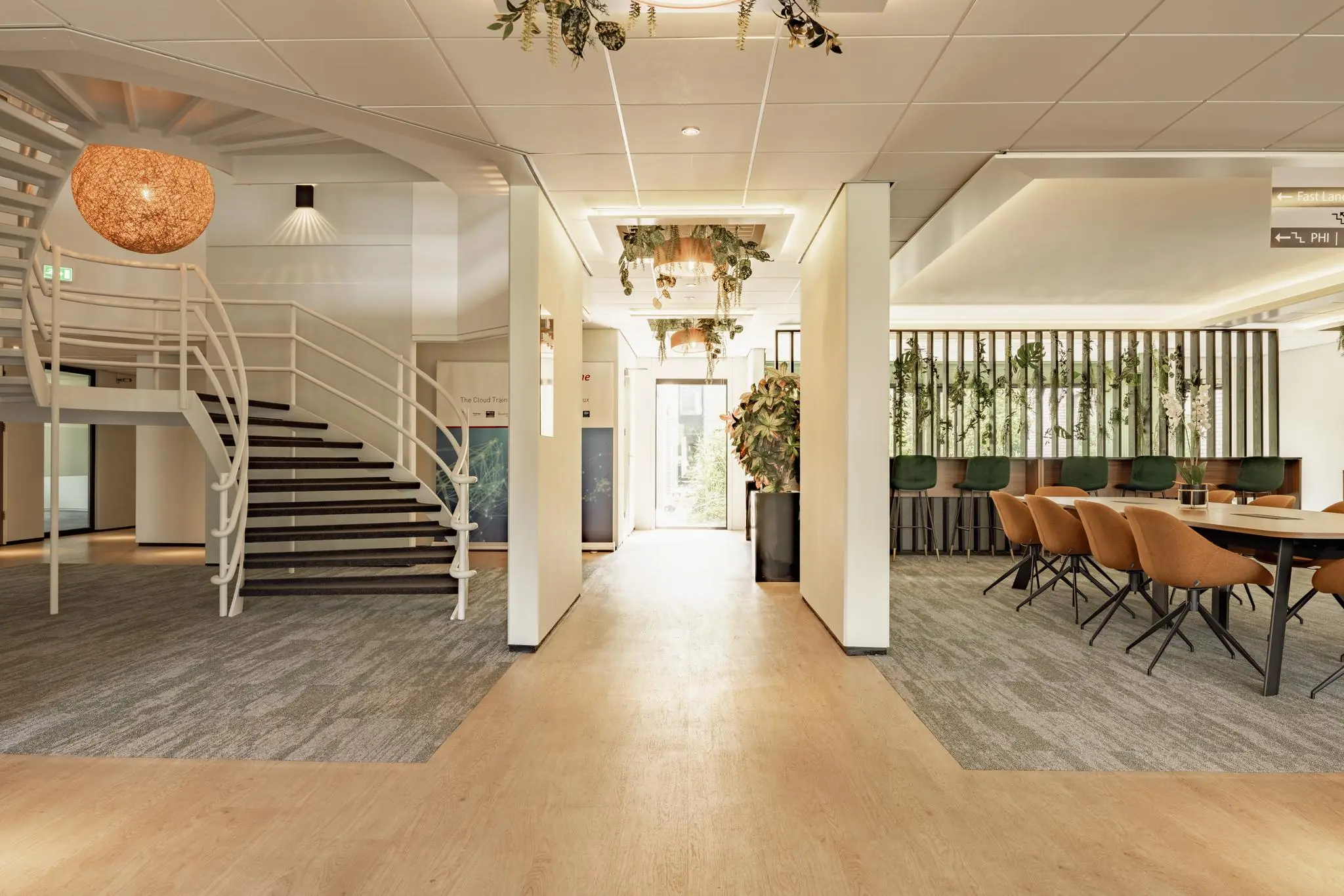 Moderne en licht ingerichte kantoorruimte met een open trap, vergadertafel en plantenwand aan de Burgemeester Verderlaan.